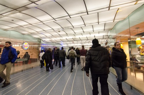 A busy indoor walkway with people walking past a Burger King, featuring a modern, curved ceiling design.