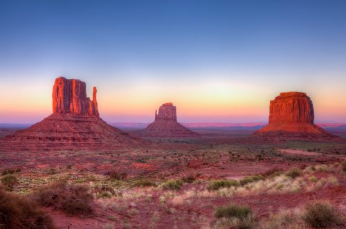 Sunset over Monument Valley, featuring iconic red rock formations and a clear blue sky.