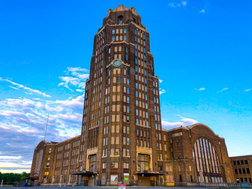 A tall, historic brick building with a clock tower, set against a blue sky with scattered clouds.