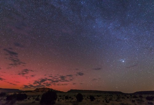 A starry night sky with a gradient of colors, featuring clouds and a distant mountain silhouette.