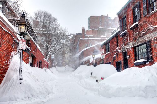 Snow-covered street with brick buildings, street lamps, and large snowdrifts, creating a wintery, quiet atmosphere.