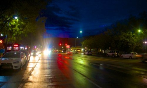A wet street at night, illuminated by streetlights and car headlights, with trees lining the road.