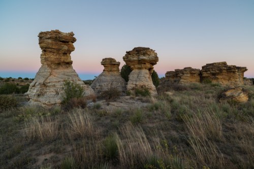 Rock formations stand in a grassy landscape at dusk, with soft pastel colors in the sky.