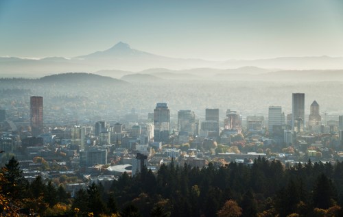 A panoramic view of a city skyline with mountains in the background, shrouded in mist and soft morning light.