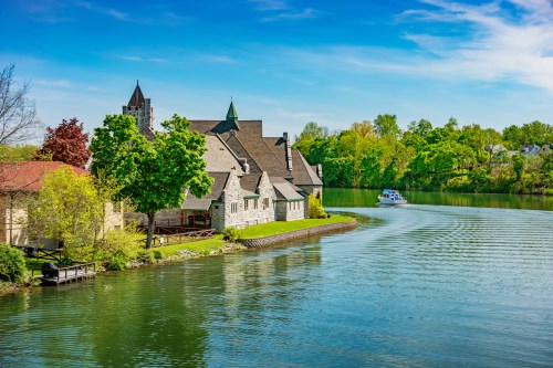 A serene lakeside view featuring a charming stone building and a boat gliding through calm waters under a blue sky.