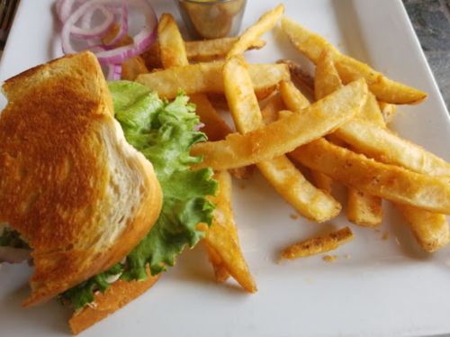 A toasted sandwich with lettuce and onion slices, served with a side of golden French fries on a white plate.