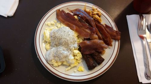 A plate of breakfast featuring scrambled eggs, sausage links, crispy bacon, and a side of gravy.