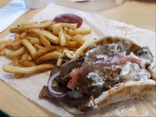 A plate featuring a pita filled with meat, tomatoes, onions, and sauce, alongside a serving of French fries and ketchup.