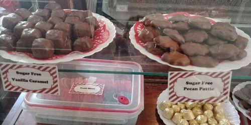 Display of sugar-free candies, including vanilla caramel and pecan patties, in a glass case with labels.