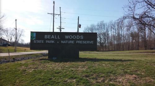 Sign for Beall Woods State Park & Nature Preserve, surrounded by grass and trees under a clear blue sky.