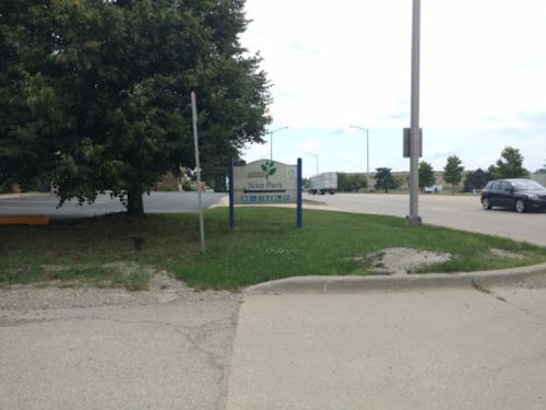 Sign for Nike Park, surrounded by trees and a road, with a car passing by in the background.