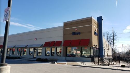 Exterior view of a building with the sign "Hive," featuring large windows and red awnings under a clear blue sky.