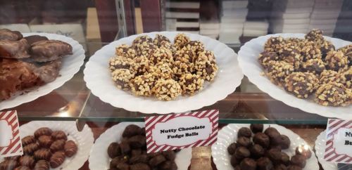 A display of various chocolates, including nutty chocolate fudge balls on a white plate, with labels underneath.