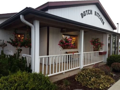 Exterior of Dutch Kitchen restaurant with flower baskets, a porch, and an "Open" sign in the window.