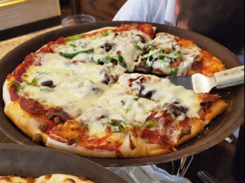 A close-up of a pizza topped with cheese, pepperoni, green peppers, and black olives, being served from a pan.
