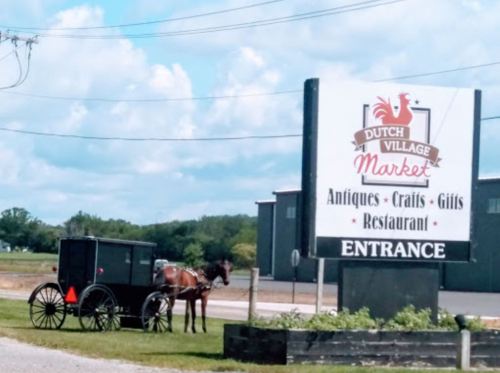 A horse and buggy parked near a sign for Dutch Village Market, featuring antiques, crafts, gifts, and a restaurant.