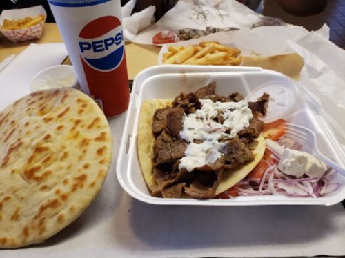 A plate with pita bread, beef, onions, tomatoes, and sauce, alongside fries and a Pepsi drink.