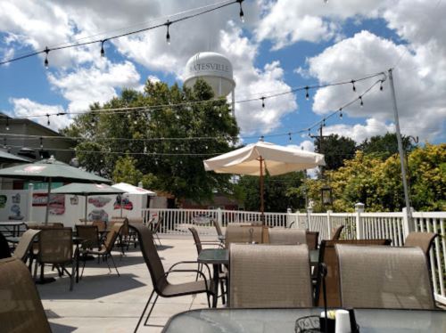 Outdoor dining area with tables, string lights, and a water tower in the background under a partly cloudy sky.