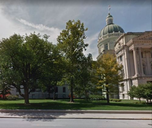 A view of a large building with a dome, surrounded by trees and green grass under a partly cloudy sky.