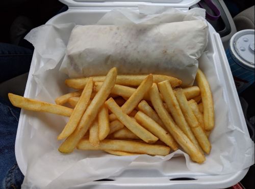 A takeout container with a wrapped burrito and a generous serving of golden French fries.
