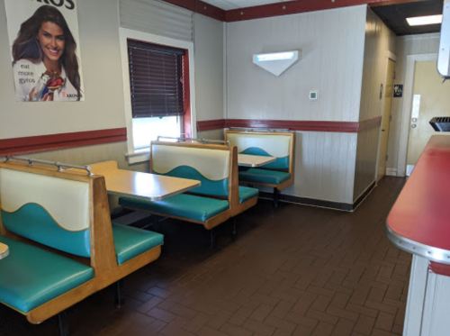 Interior of a diner with teal booths and tables, featuring a poster on the wall and a doorway in the background.