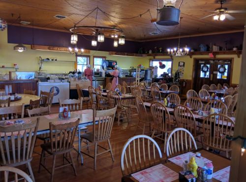 Cozy restaurant interior with wooden tables and chairs, featuring a counter and kitchen area in the background.