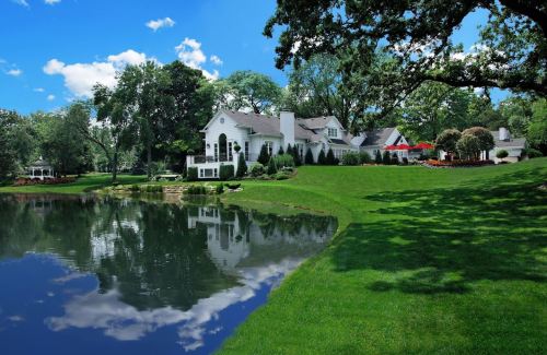 A picturesque house by a serene pond, surrounded by lush greenery and blue skies with fluffy clouds.