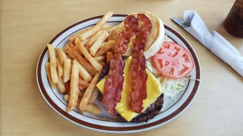 A cheeseburger topped with bacon, lettuce, and tomato, served with a side of fries on a plate.