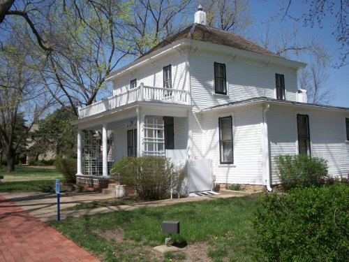 A white two-story house with a porch, surrounded by greenery and a clear blue sky.