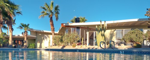 A serene pool scene with palm trees, a modern house, and clear blue skies reflecting in the water.
