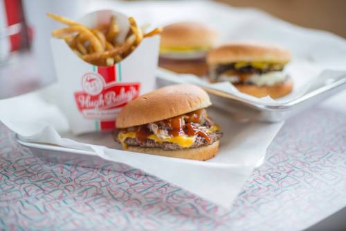 A close-up of a juicy burger with cheese and sauce, accompanied by a side of fries in a takeout container.