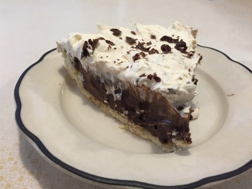 A slice of chocolate cream pie topped with whipped cream and chocolate shavings on a white plate.