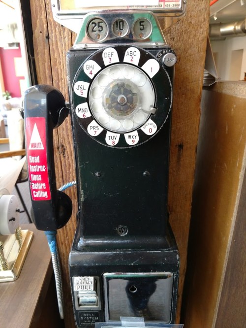 A vintage payphone with a rotary dial and a coin slot, mounted on a wooden wall.