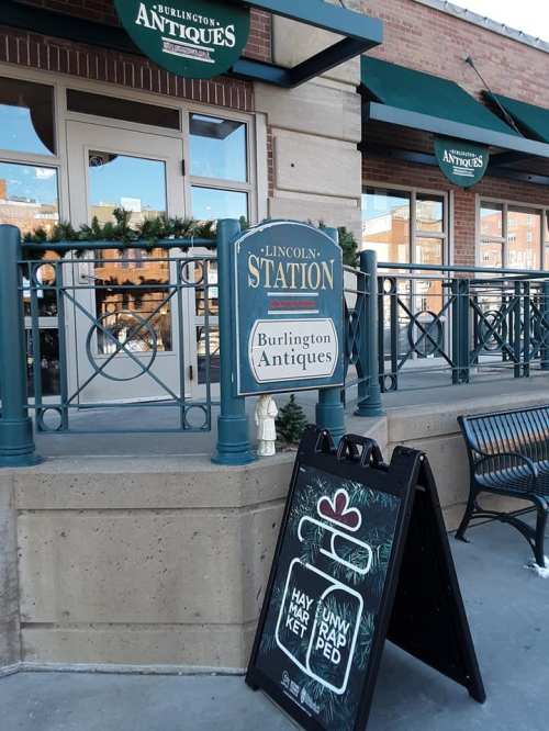 Sign for Burlington Antiques outside Lincoln Station, featuring a holiday market announcement on a sidewalk board.