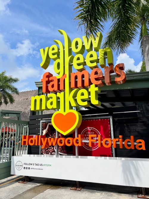 Colorful sign for the Yellow Green Farmers Market in Hollywood, Florida, with palm trees in the background.