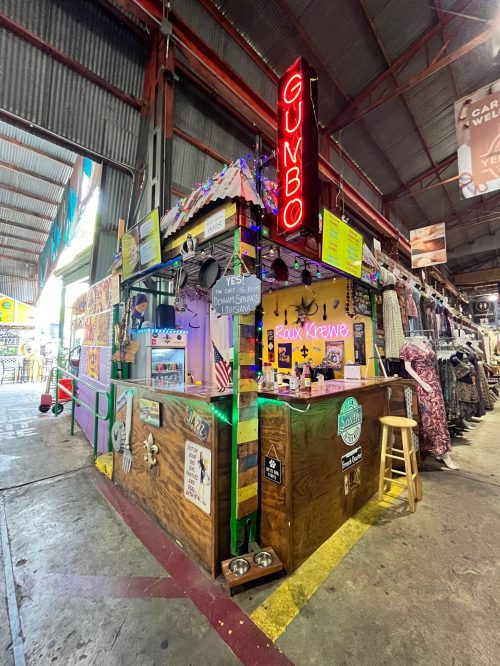 Colorful food stall named "Gumbo" with festive decorations, located in a bustling market.