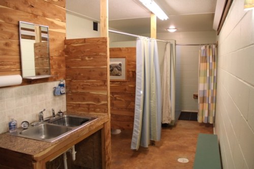 A rustic bathroom with wooden walls, a sink, and two shower stalls separated by curtains.