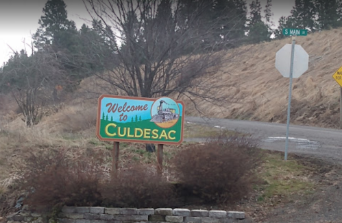 Welcome sign for Culdesac, with a road sign indicating South Main Street nearby. Trees and dry grass in the background.