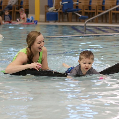 A woman and a young boy swim together in a pool, both smiling and enjoying the water.