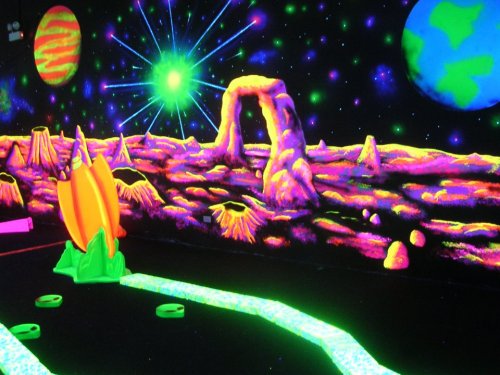 A vibrant, neon-colored mini-golf course with a cosmic space theme, featuring planets and glowing landscapes.