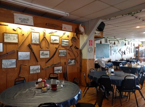 A rustic dining area with round tables, featuring a wall adorned with historical photos and vintage tools.