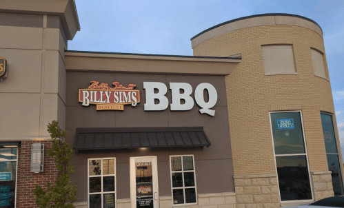 Sign for Billy Sims BBQ on a restaurant building, featuring a brown facade and large white lettering.