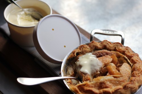 A slice of apple pie with a scoop of vanilla ice cream in a cup, served on a wooden table.
