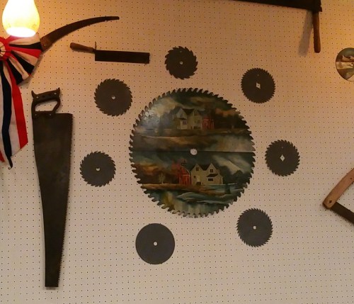 A wall display featuring various saw blades and tools, with a painted circular saw depicting a scenic landscape.