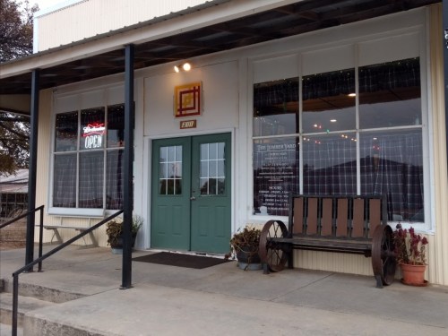 A storefront with large windows, a green door, and a bench outside, featuring an "Open" sign and decorative elements.