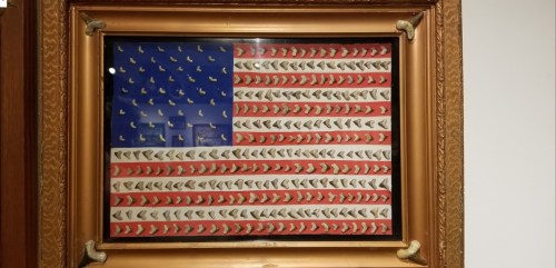 A framed artwork resembling the American flag, made of small white objects arranged in stripes and a blue field.