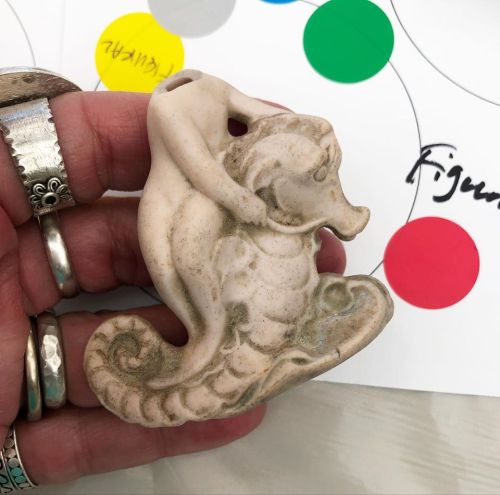 A hand holding a carved seahorse figurine with a small figure on its back, surrounded by colorful dots and notes.