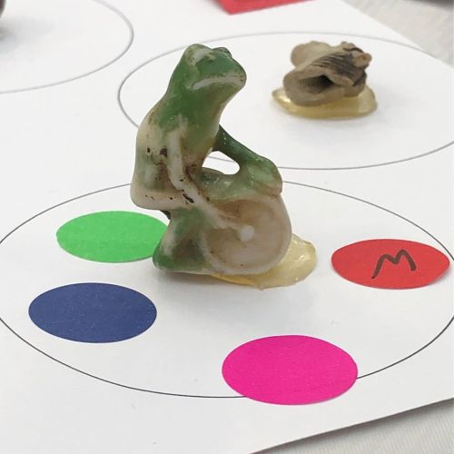 A small, intricately carved figurine of a seated frog on a colorful circular background.