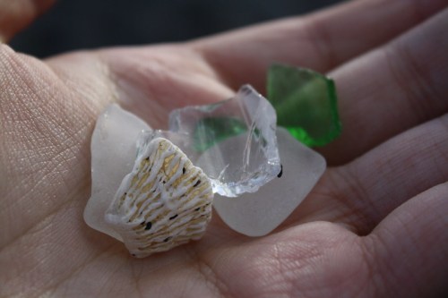 A hand holding a collection of colorful sea glass pieces, including white, green, and clear fragments.