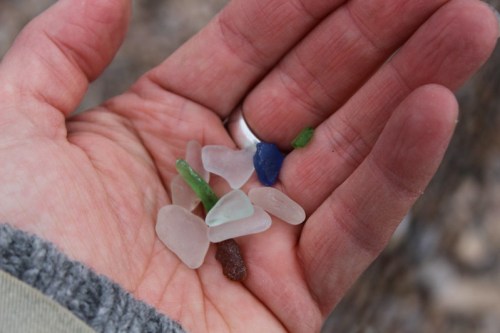 A hand holding a collection of colorful sea glass pieces in various shapes and sizes.